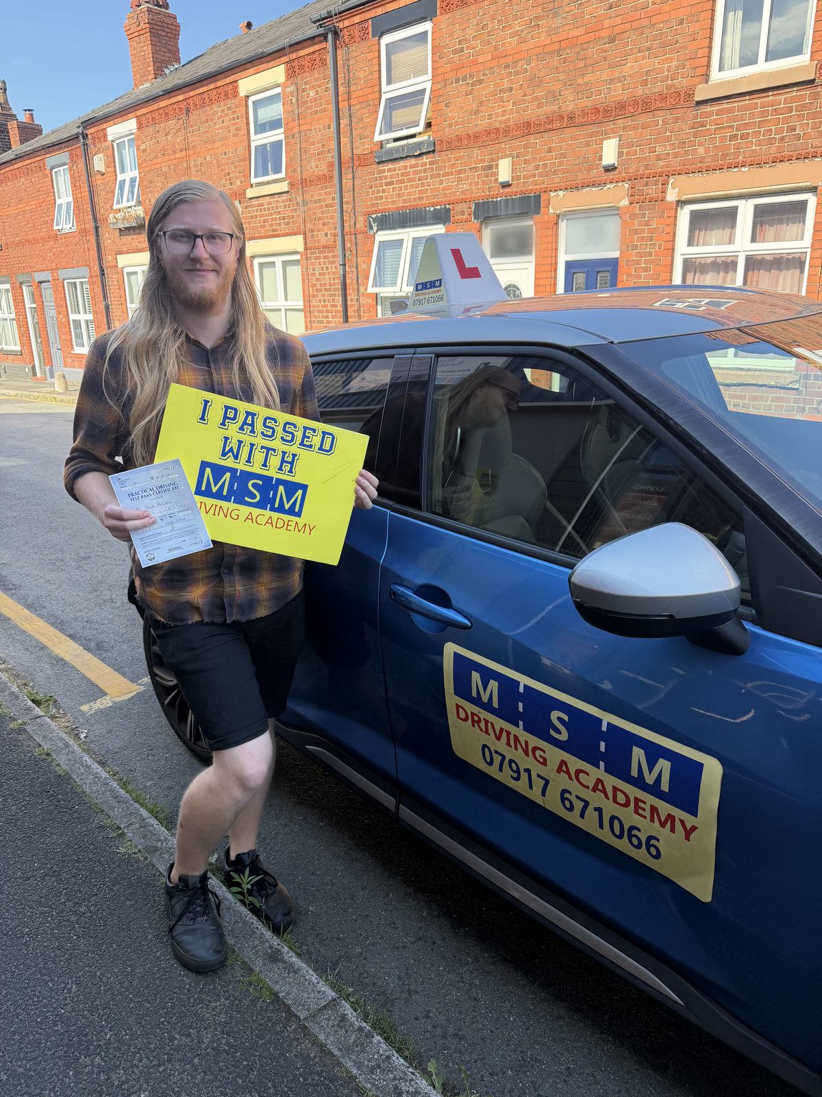A learner celebrating with his pass certificate beside an MSM Driving Academy car in Warrington